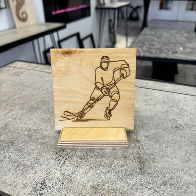 laser engraved image featuring a line drawing of a hockey player displayed on a baltic birch tile with a baltic birch stand